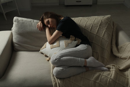 Sad young woman lying on sofa at homeの写真素材