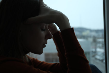 Sad young woman near window at home, closeupの写真素材