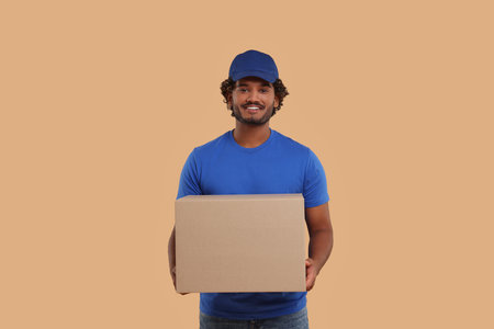 Happy young courier with parcel on light brown background