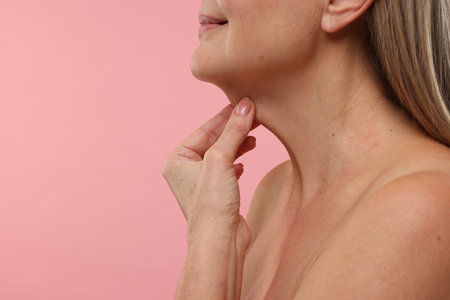 Mature woman touching her neck on pink background, closeup. Space for textの写真素材