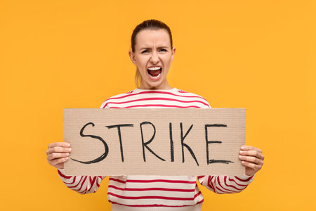 Screaming woman holding cardboard banner with word Strike on orange background