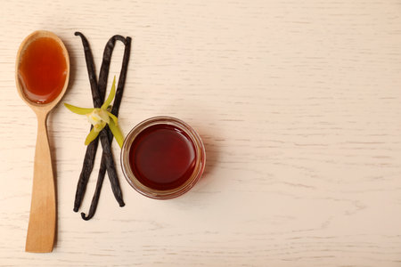Aromatic vanilla extract, pods and flower on white wooden table, flat lay. Space for text