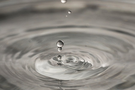 Drops falling into clear water on gray background, closeupの写真素材