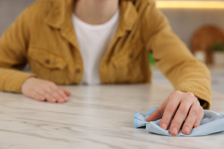 Woman with microfiber cloth cleaning white marble table in kitchen, closeupの写真素材