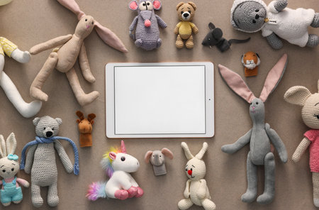 Modern tablet and kid's toys on light brown background, flat lay. Space for text