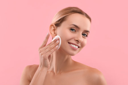 Smiling woman removing makeup with cotton pad on pink backgroundの写真素材