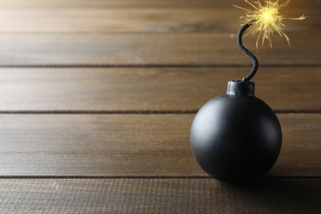 Old fashioned black bomb with lit fuse on wooden table, space for textの写真素材