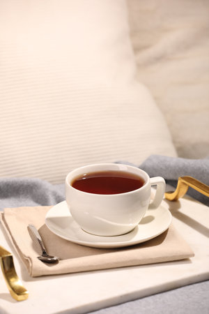 Aromatic tea in cup, saucer and spoon on bedの写真素材