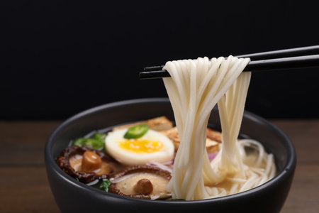 Eating delicious vegetarian ramen with chopsticks at table against black background, closeupの写真素材