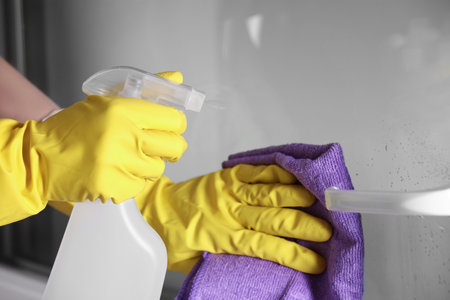 Woman with spray bottle and microfiber cloth cleaning window, closeup