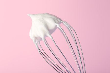Whisk with whipped egg whites on pink background, closeupの写真素材
