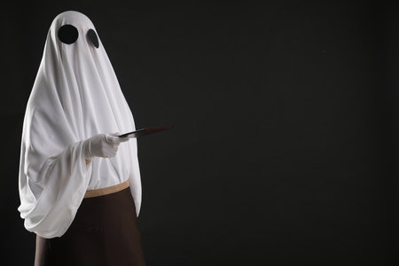 Creepy ghost. Waiter in white sheet and apron with receipt on black background, space for textの写真素材