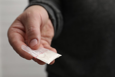 Drug addiction. Man with plastic bag of cocaine on light background, closeup