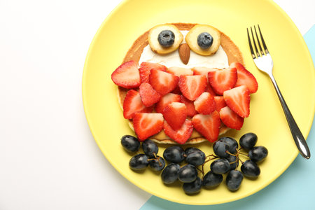 Creative serving for kids. Plate with cute owl made of pancakes, berries, cream, banana and almond on color background, top view. Space for textの写真素材