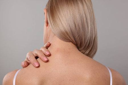 Woman suffering from pain in her neck on gray background, back viewの写真素材