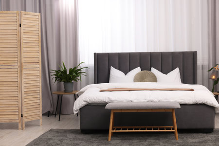Stylish bedroom interior with large bed, ottoman, lamp and houseplantsの写真素材