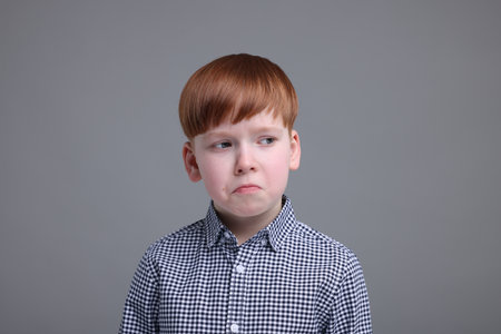 Portrait of sad little boy on gray background