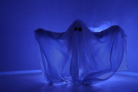 Creepy ghost. Woman covered with sheet in blue lightの写真素材