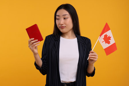 Immigration to Canada. Woman with passport and flag on orange backgroundの写真素材