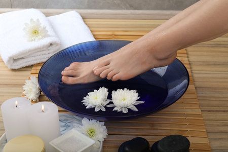 Woman soaking her feet in bowl with water and flowers on floor, closeup. Spa treatmentの写真素材