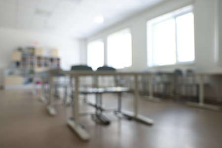 Blurred view of empty school classroom with desks, windows and chairsの写真素材
