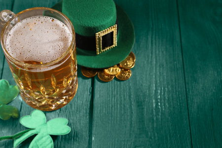 St. Patrick's day. Beer, leprechaun hat, gold and decorative clover leaves on green wooden table....