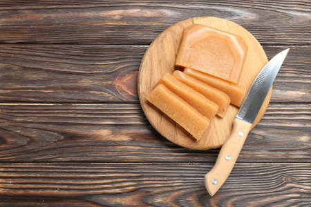 Tasty sweet quince paste and knife on wooden table, top view. Space for text