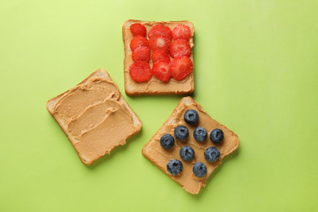 Tasty peanut butter sandwiches with fresh berries on light green background, flat layの写真素材