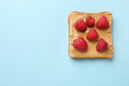 Tasty peanut butter sandwich with fresh raspberries on light blue background, top view. Space for textの写真素材