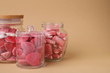 Tasty pink candies in glass jars on beige background, space for textの写真素材
