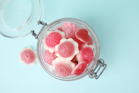 Tasty pink candies in glass jar on light blue background, top view