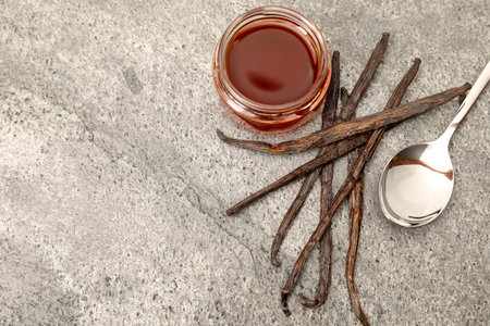 Aromatic vanilla extract and pods on gray table, flat lay. Space for text