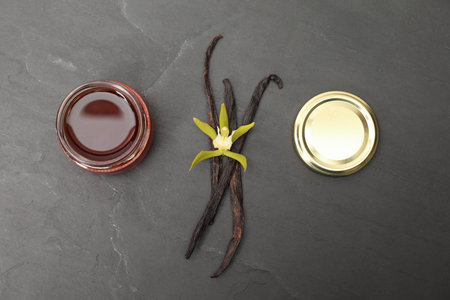 Aromatic vanilla extract, pods and flower on black table, flat lay
