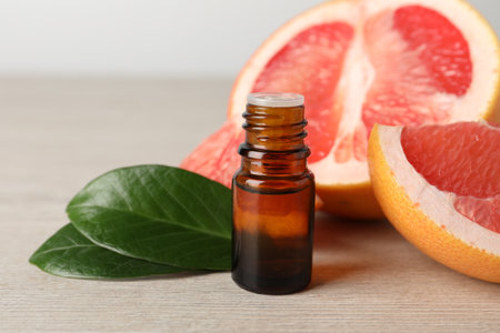 Grapefruit essential oil in bottle, leaves and fruit on light wooden table, closeupの写真素材