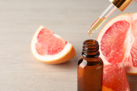 Dripping grapefruit essential oil from pipette into bottle and fresh fruit on wooden table, closeup. Space for textの写真素材