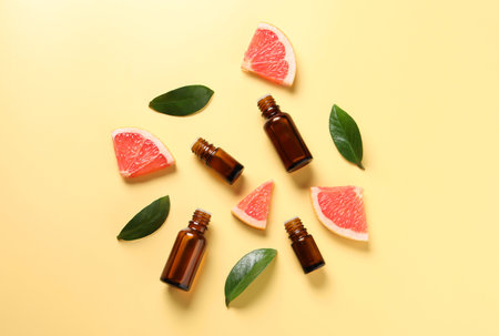 Grapefruit essential oil in bottles, leaves and cut fruit on yellow table, flat layの写真素材