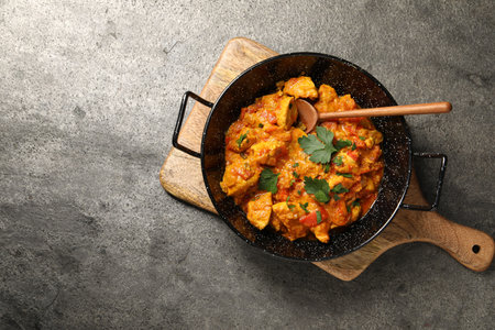 Delicious chicken curry in frying pan and spoon on gray table, top view. Space for textの写真素材