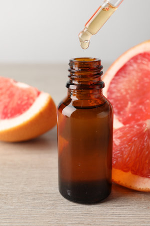 Dripping grapefruit essential oil from pipette into bottle and fresh fruit on light wooden table, closeupの写真素材