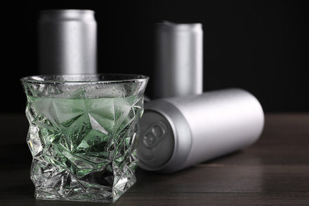 Energy drink in glass and aluminum cans on wooden table, closeup. Space for text