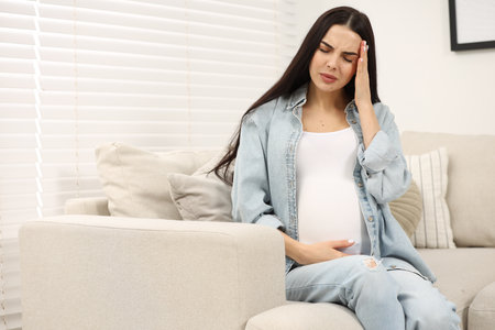 Pregnant woman suffering from headache on sofa at homeの写真素材