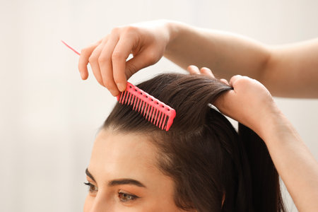Hair styling. Professional hairdresser combing woman's hair indoors, closeupの写真素材