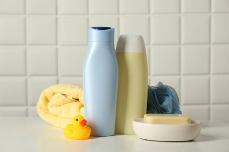 Baby cosmetic products, bath duck, sponge and towel on white table against tiled wall
