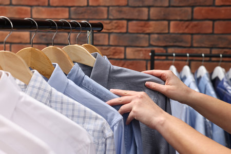 Dry-cleaning service. Woman taking shirt from rack against brick wall, closeupの写真素材