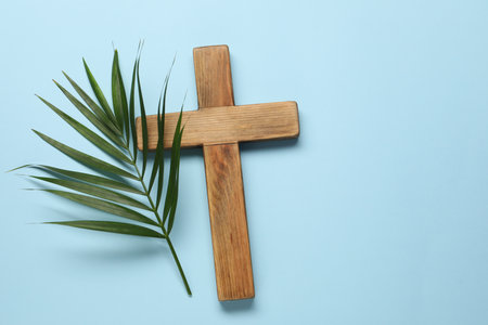 Wooden cross and palm leaf on light blue background, top view with space for text. Easter attributesの写真素材