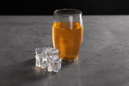 Energy drink in glass and ice cubes on gray table