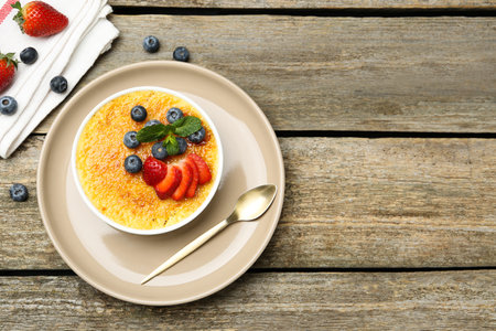 Delicious creme brulee with berries and mint in bowl on wooden table, top view. Space for textの写真素材
