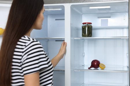 Young woman near empty refrigerator indoors, selective focusの写真素材
