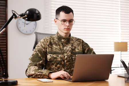 Military service. Young soldier working with laptop at wooden table in officeの写真素材