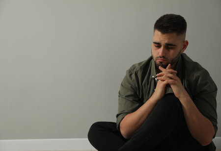 Sad man sitting near light gray wall. Space for text