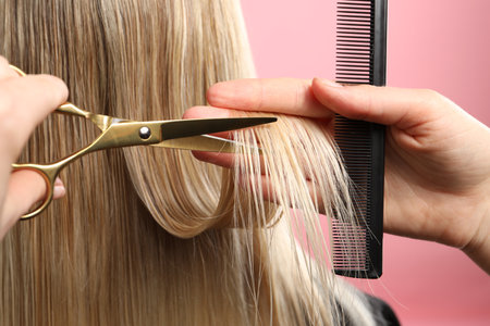 Hairdresser cutting client's hair with scissors on pink background, closeupの写真素材